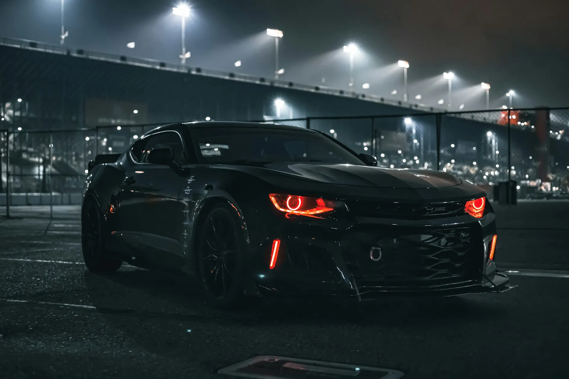 Black muscle car with glowing red headlights at night.