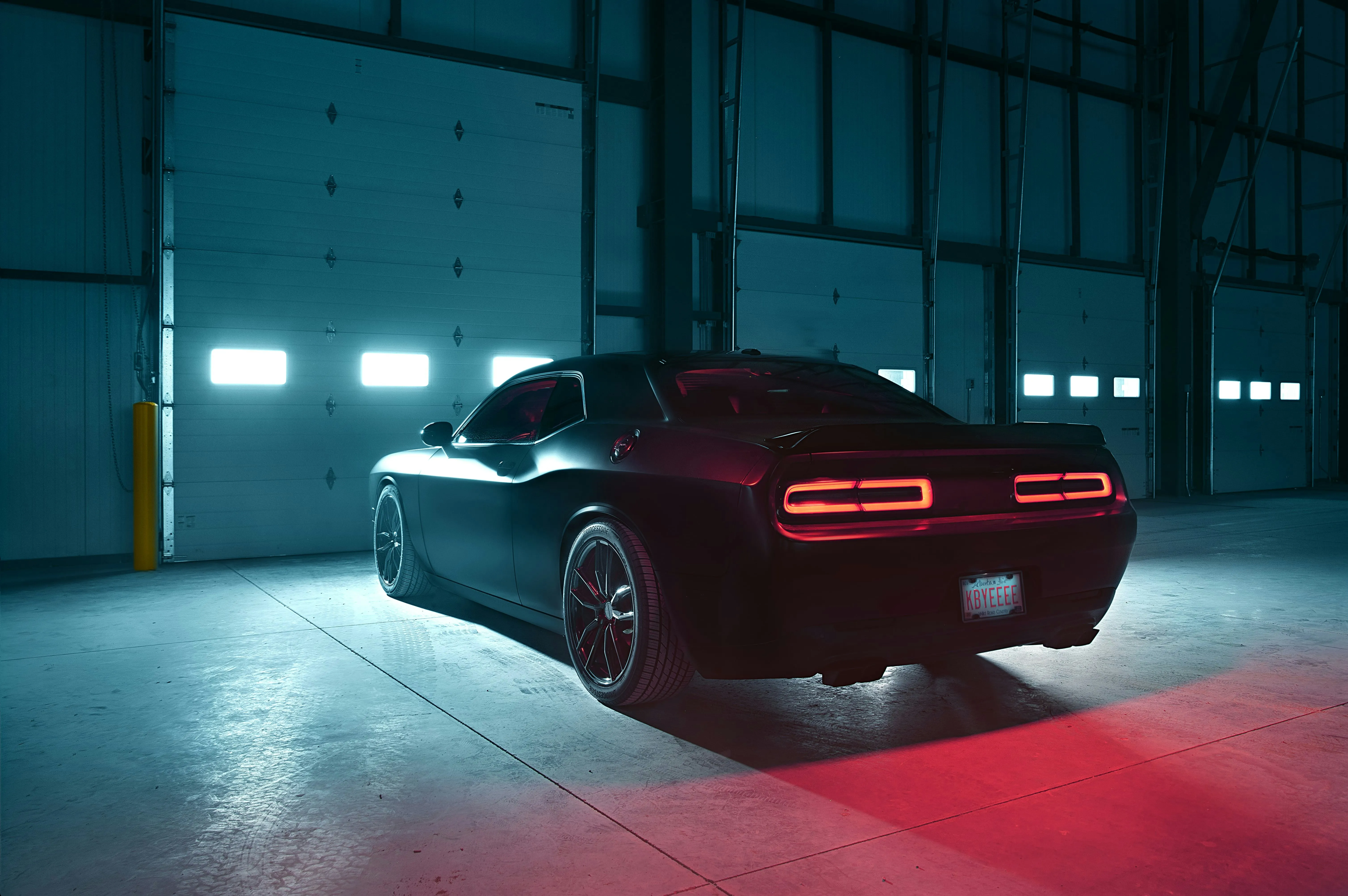 Black muscle car, rear view, in a dimly lit warehouse
